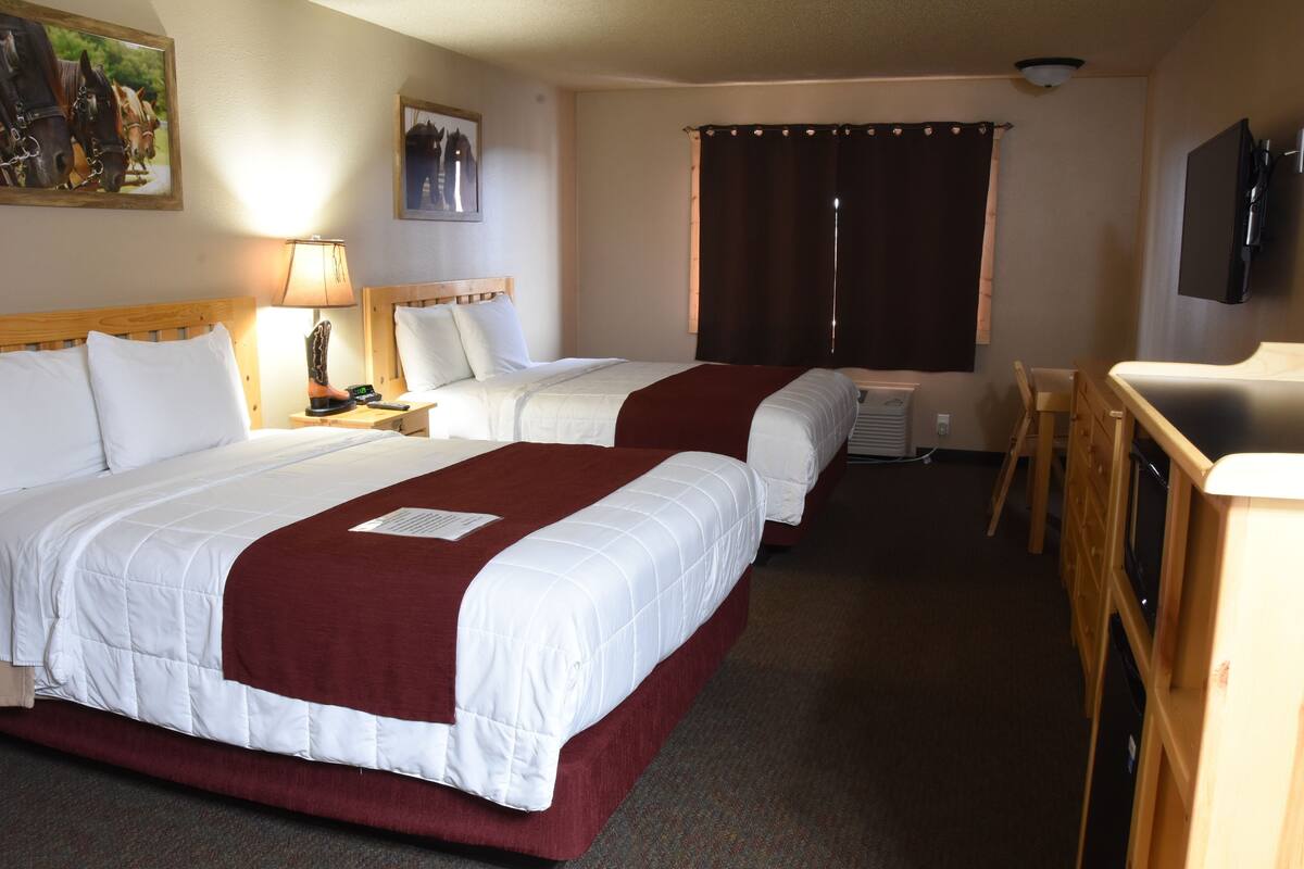 A hotel room with two beds, a desk, a chair, a TV, and a window with curtains.