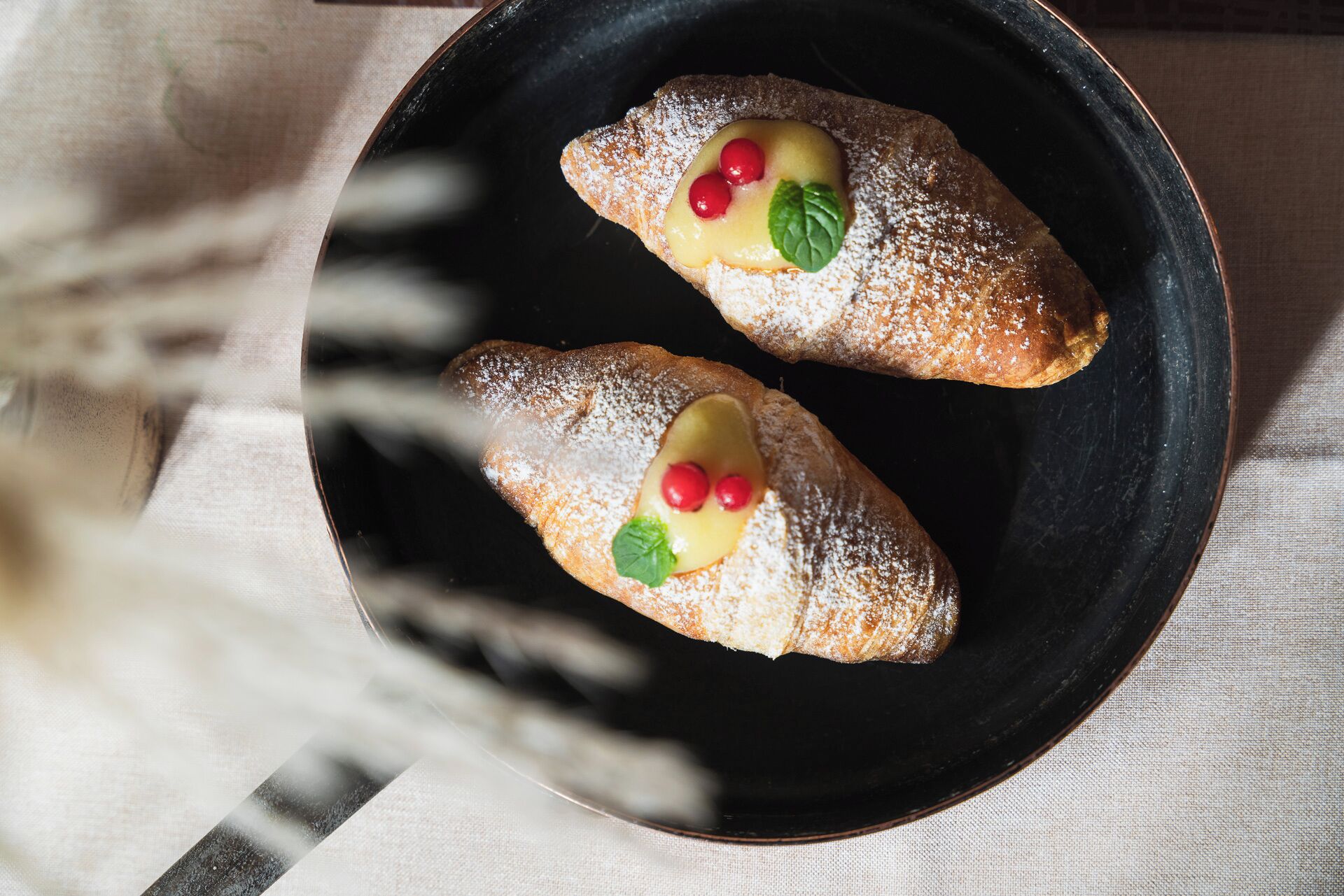 Two pastries on a black plate, dusted with powdered sugar, with a blurred background.