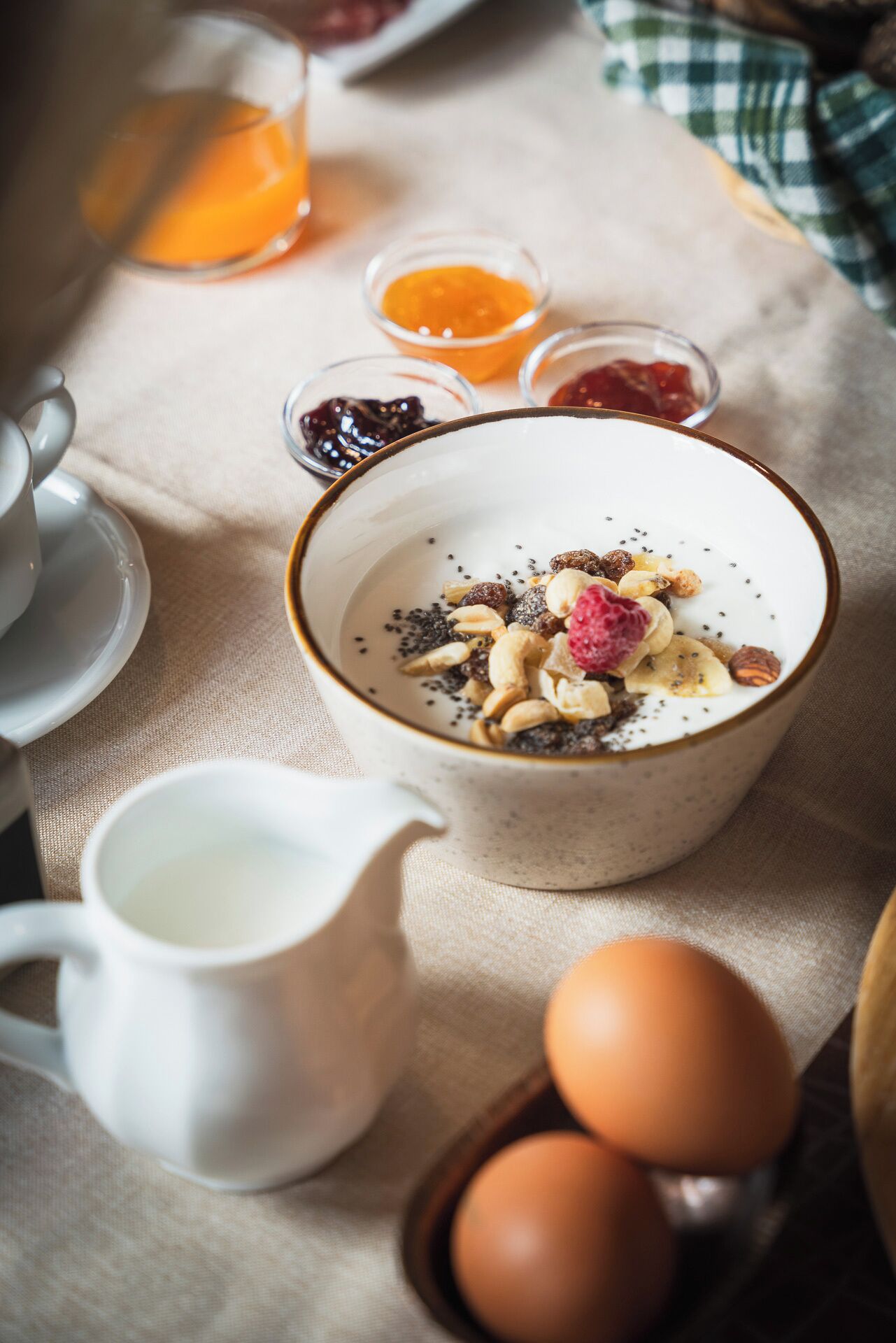 Un desayuno con un tazón de cereal cubierto de frutas y nueces, una jarra de leche y un plato con huevos.