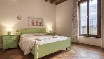 A bedroom with a green bed, two bedside tables, a nightstand, a window with curtains, and a painting on the wall.