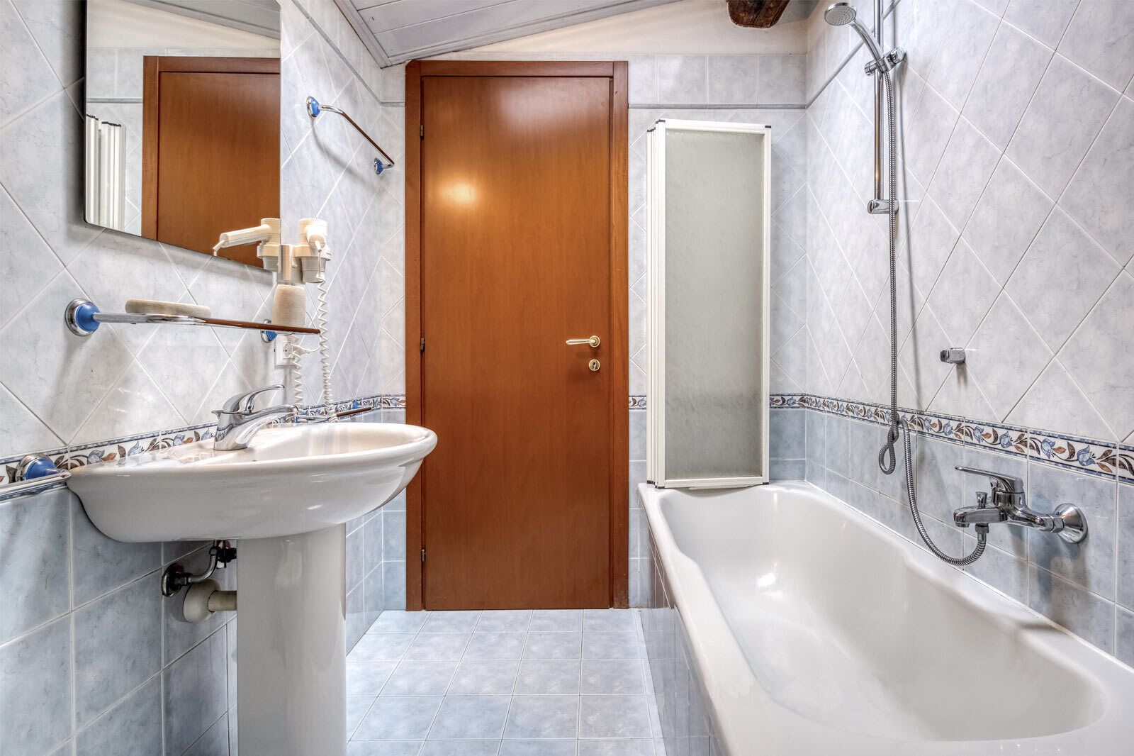 Een badkamer met een wastafel, spiegel, douche en een houten deur.