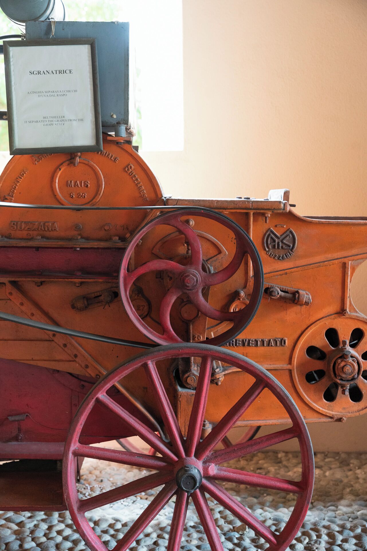 An antique tractor with red wheels and a plaque reading "Sgranatrice" and "A Cinghia Separava I Cichii D'uva dal Raspo".