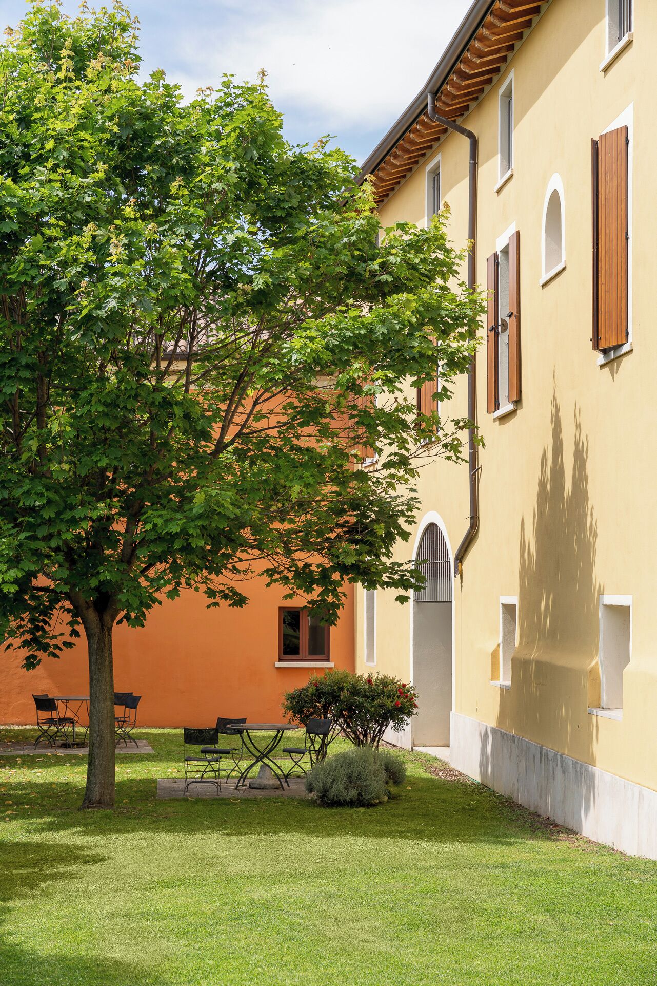 A building with a yellow facade, a tree in the foreground, and a patio area with outdoor furniture.