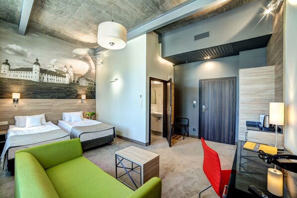 A hotel room with two beds, a green sofa, a desk with a lamp, and a bathroom visible through an open door. - Hotel Loft 1898 (Suwalki)
