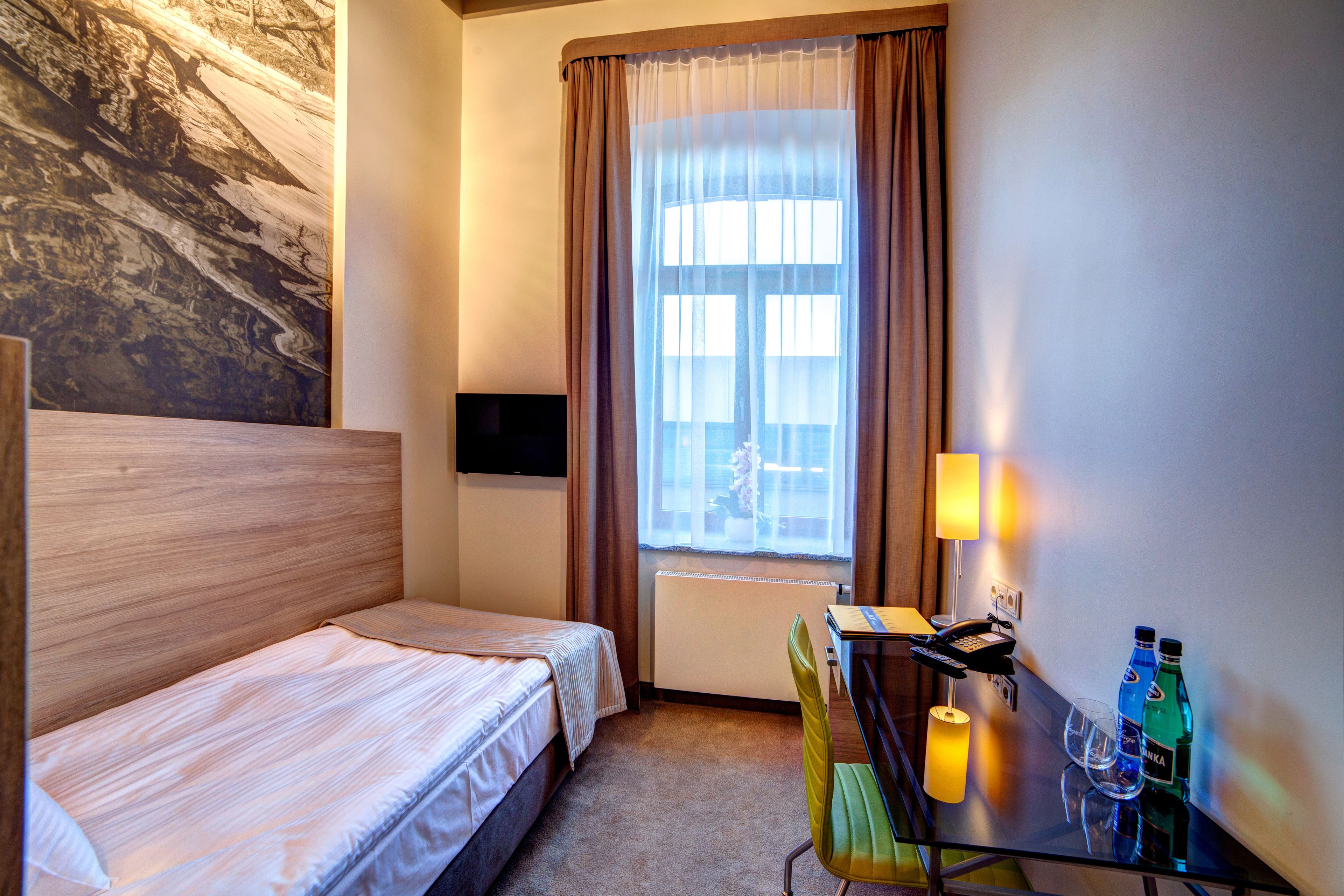 Habitación de hotel con una cama, un escritorio con una silla, una lámpara y dos botellas de agua.