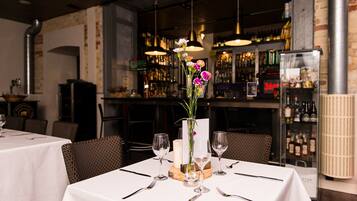 L'intérieur d'un restaurant, avec des tables dressées pour le service, un bar en arrière-plan et un vase décoratif rempli de fleurs posé sur une table.