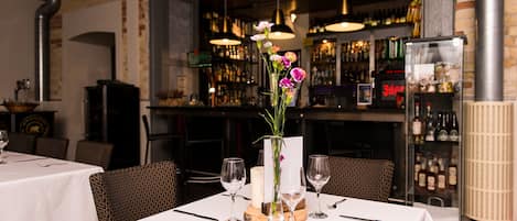 Interior de restaurante con mesas dispuestas para comer, una zona de bar al fondo y un jarrón decorativo con flores en la mesa.