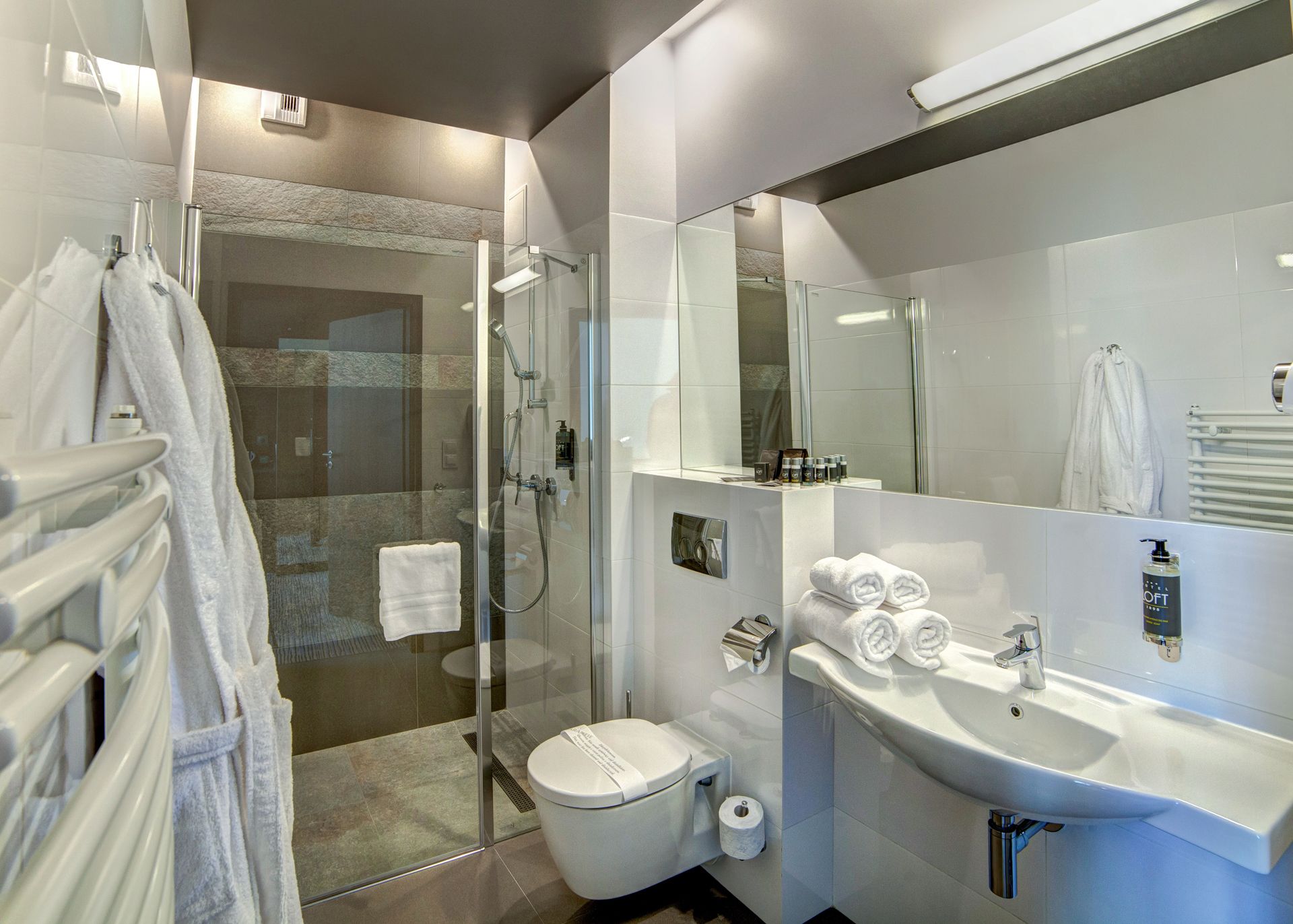 Ein modernes Badezimmer mit einer Duschkabine, einer Toilette, einem Waschbecken mit Spiegel und ordentlich drapierten Handtüchern.