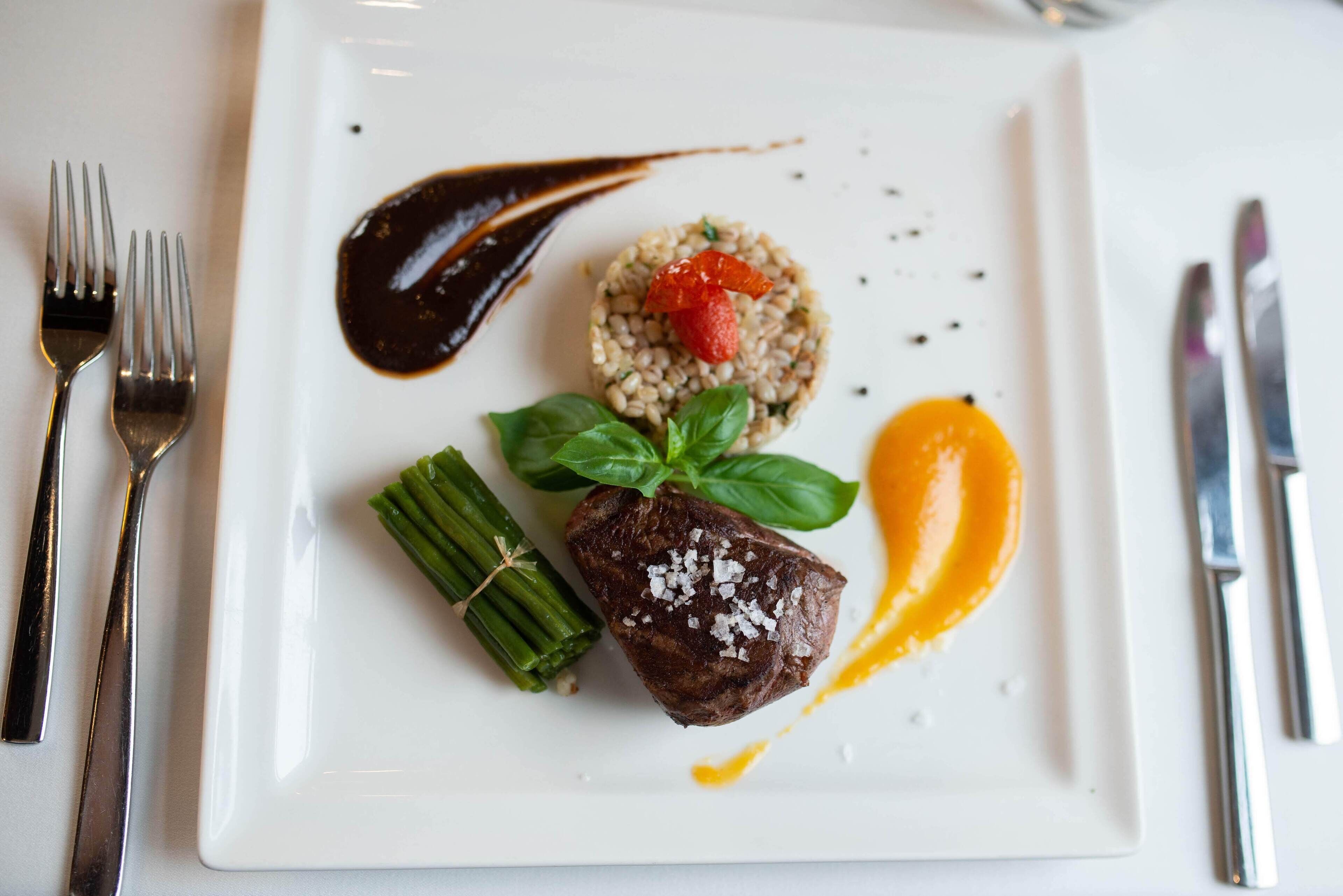 A white plate with a steak, green beans, and a side of orange.