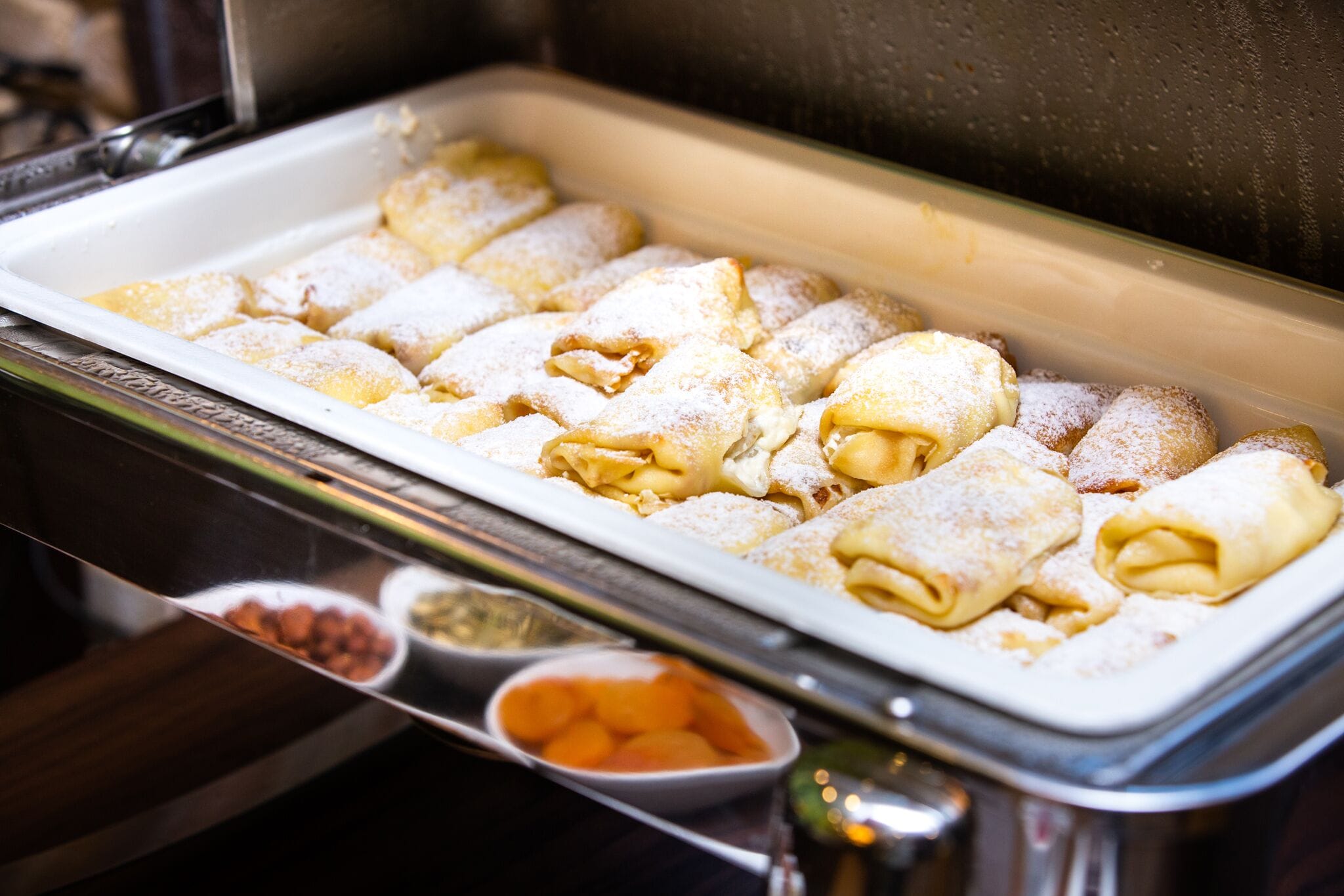 A buffet with a variety of pastries, including rolled doughnuts and other sweet treats, dusted with powdered sugar.