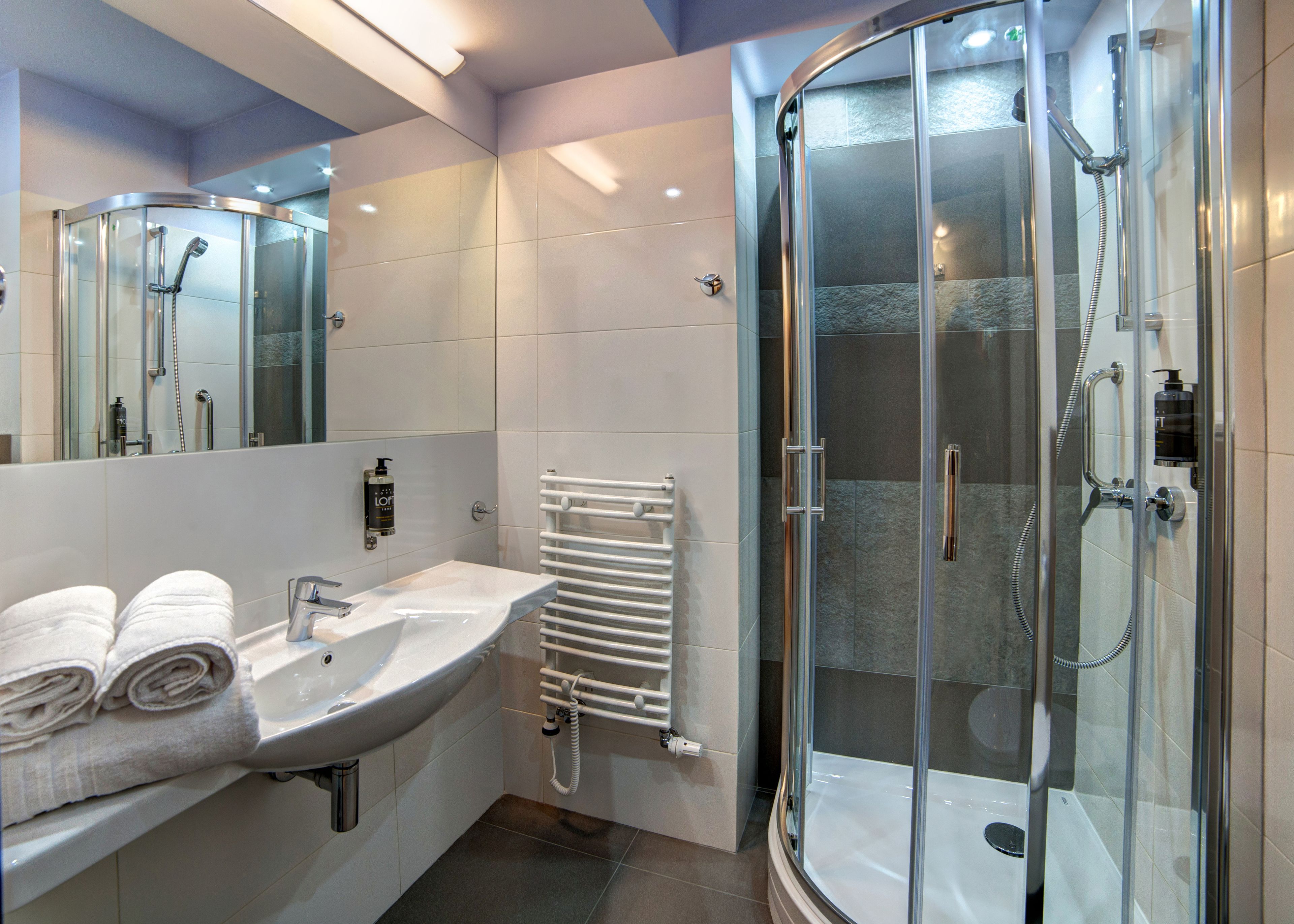 A modern bathroom with a glass-enclosed shower, a white sink, and a towel rack.