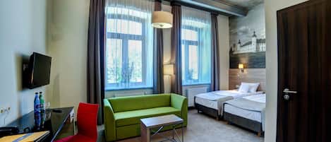 A hotel room with a bed, a green sofa, a desk with a computer, a TV, and a window with curtains.