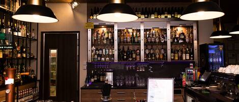 Zona de bar con estantes llenos de botellas de licor, una caja registradora y un monitor de computadora.