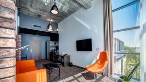 A modern living room with a large window, a flat-screen TV, and orange furniture. - Hotel Loft 1898 (Suwalki)