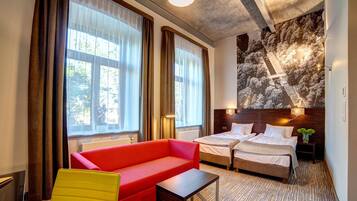 Een hotelkamer met een rode bank, twee bedden, een kleine tafel en een groot muurschildering.