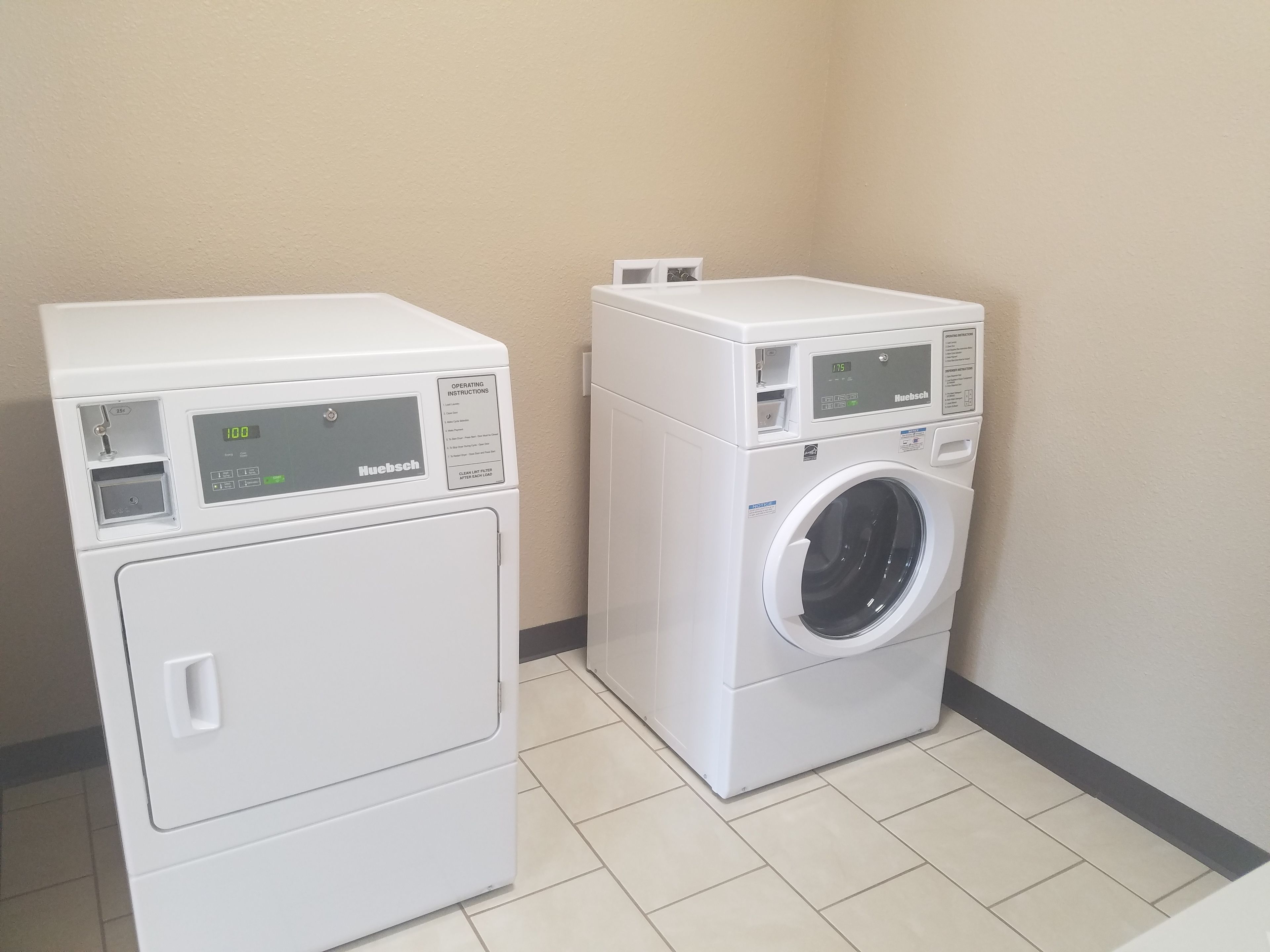 A laundry room with two white appliances, one dryer and one washer, with control panels and a power outlet.