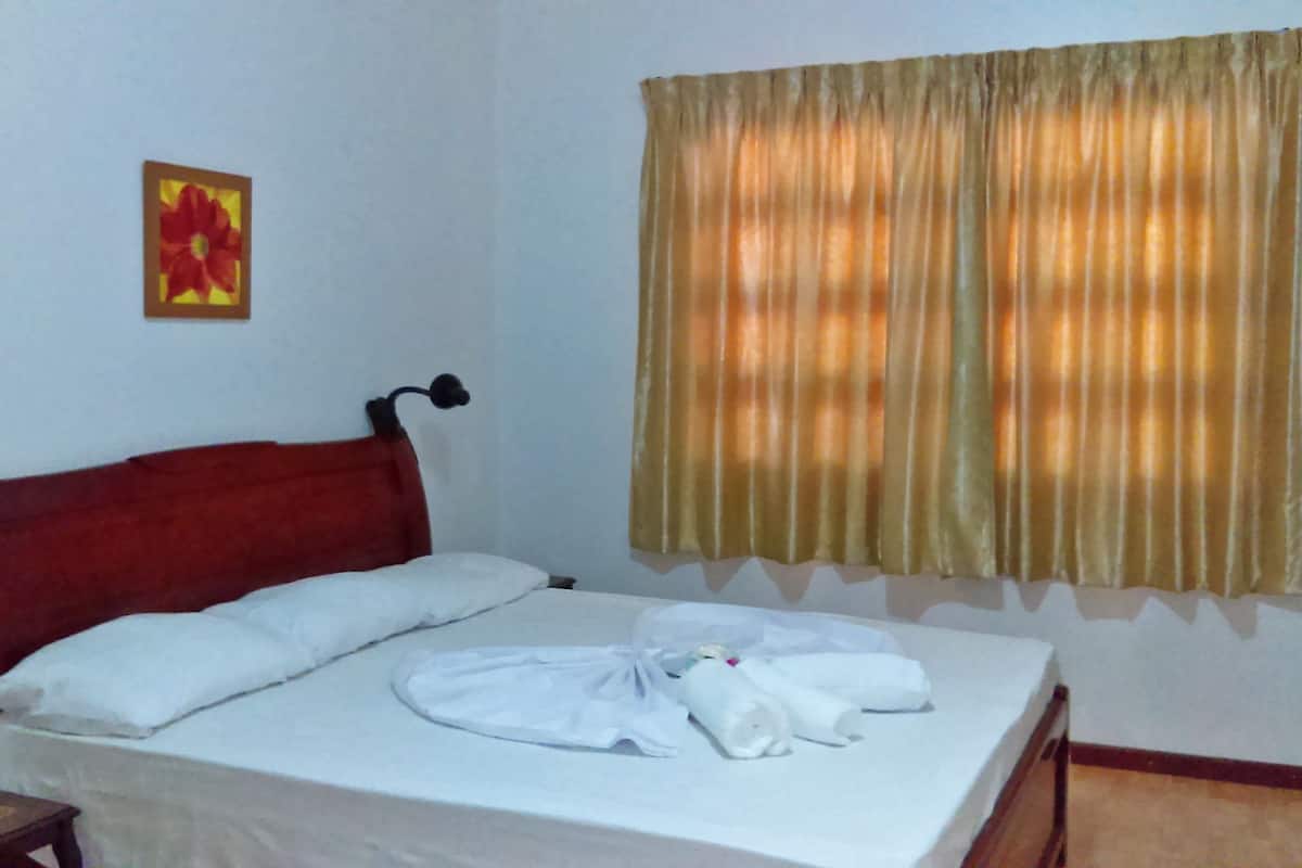 Una cama bien hecha con sábanas blancas, un cabecero rojo y una única almohada blanca.