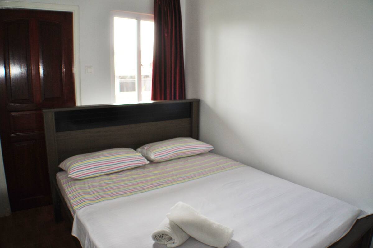 Una cama bien hecha con ropa de cama a rayas y dos almohadas, un cabecero de madera y una ventana con cortinas.