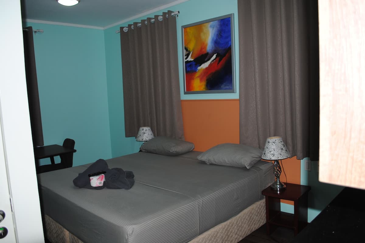 Una habitación de hotel con una cama, dos mesitas de noche, una silla y un cuadro en la pared.
