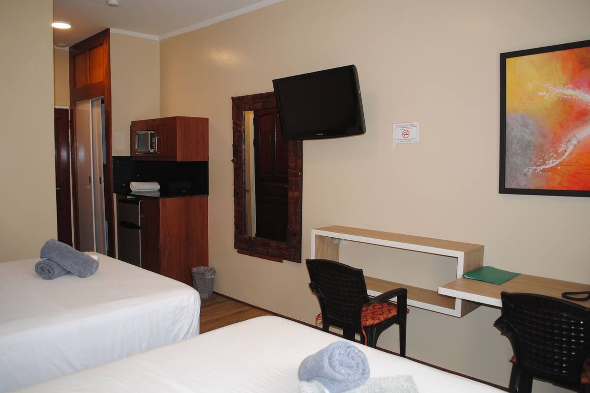 Habitación de hotel con dos camas, un escritorio, una silla, un televisor montado en la pared y un microondas en la kitchenette.