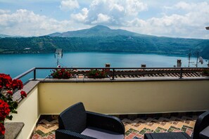 A terrace with wicker furniture, a view of a lake, and mountains in the background.