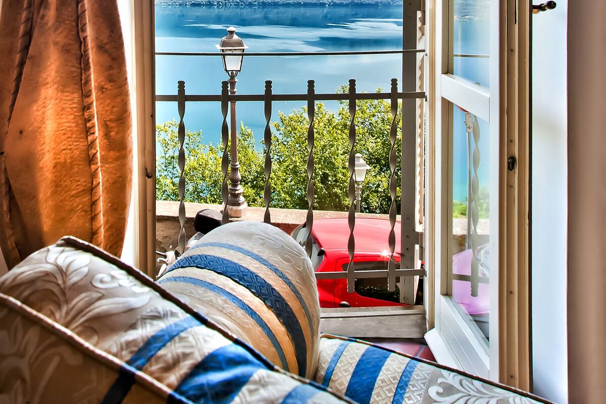 A balcony with a view of a lake and mountains, a red car parked outside, and a lamp post.