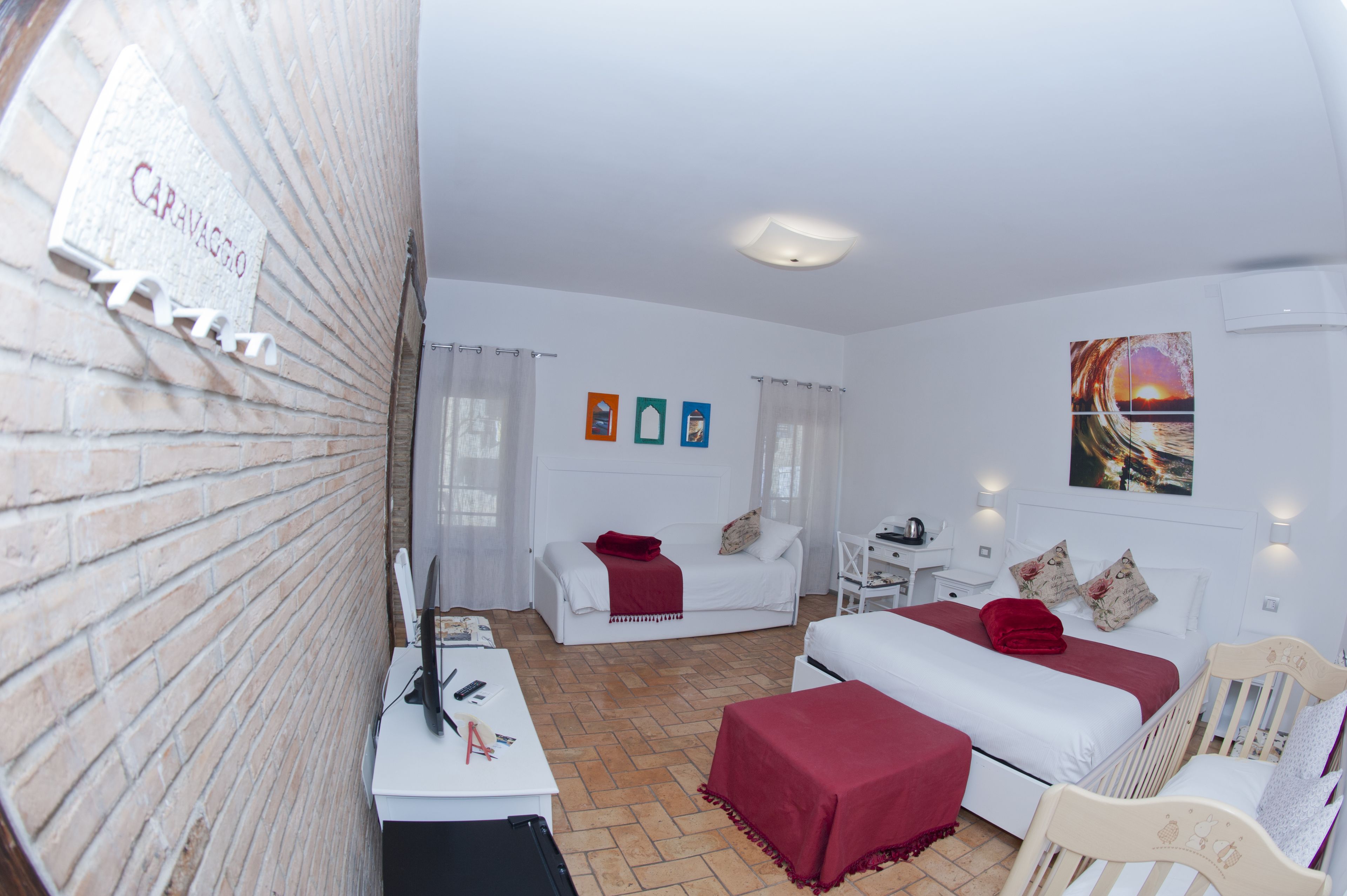 Ein Hotelzimmer mit Backsteinwand, einem weißen Bett, einem weißen Sofa, einem Schreibtisch mit Computer und einem Gemälde einer Sonnenuntergangslandschaft.