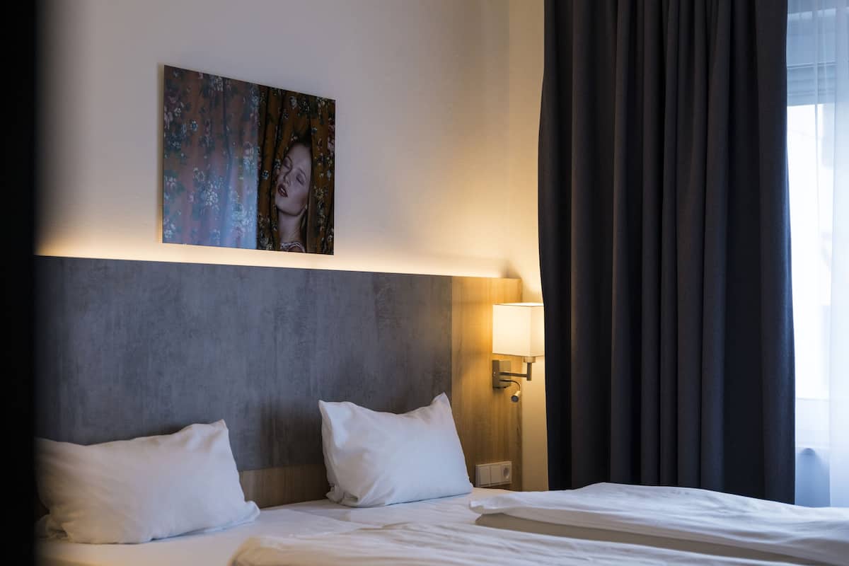 Ein Hotelzimmer mit einem großen Bett, einem Kopfteil, einer Wandlampe und einem Gemälde über dem Bett.