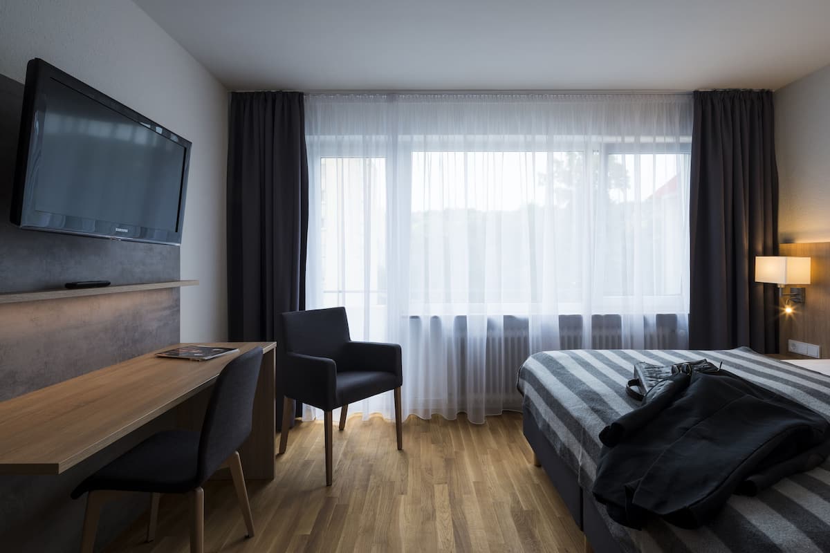 Ein Hotelzimmer mit Bett, Schreibtisch, Stuhl, Fernseher und einem Fenster mit Vorhängen.