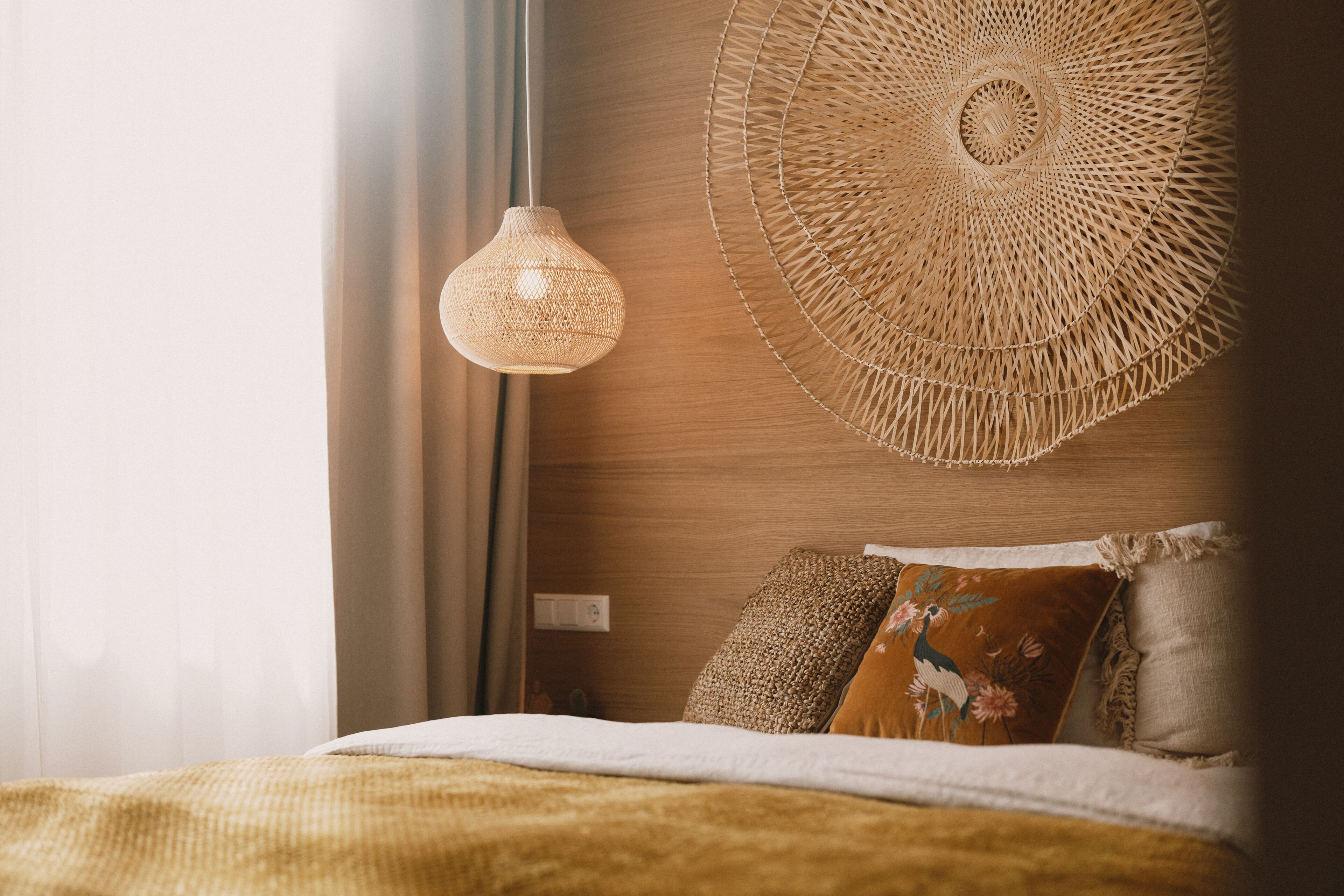 A neatly arranged bedroom with a bed, a hanging woven light fixture, and a wall-mounted woven decorative piece.