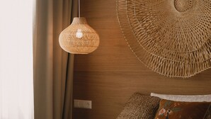 A bedroom with a bed, a hanging woven light fixture, a large woven wall art piece, and a brown textured pillow. -  2Places Side (Loerrach)