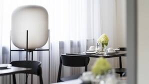 A modern dining area with a round table, black chairs, and a white table lamp. -  2Places Side (Loerrach)
