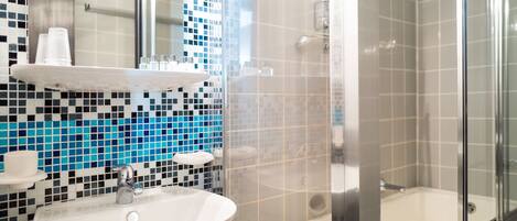 Un baño con lavamanos blanco, un espejo y zona de ducha con puerta de cristal.