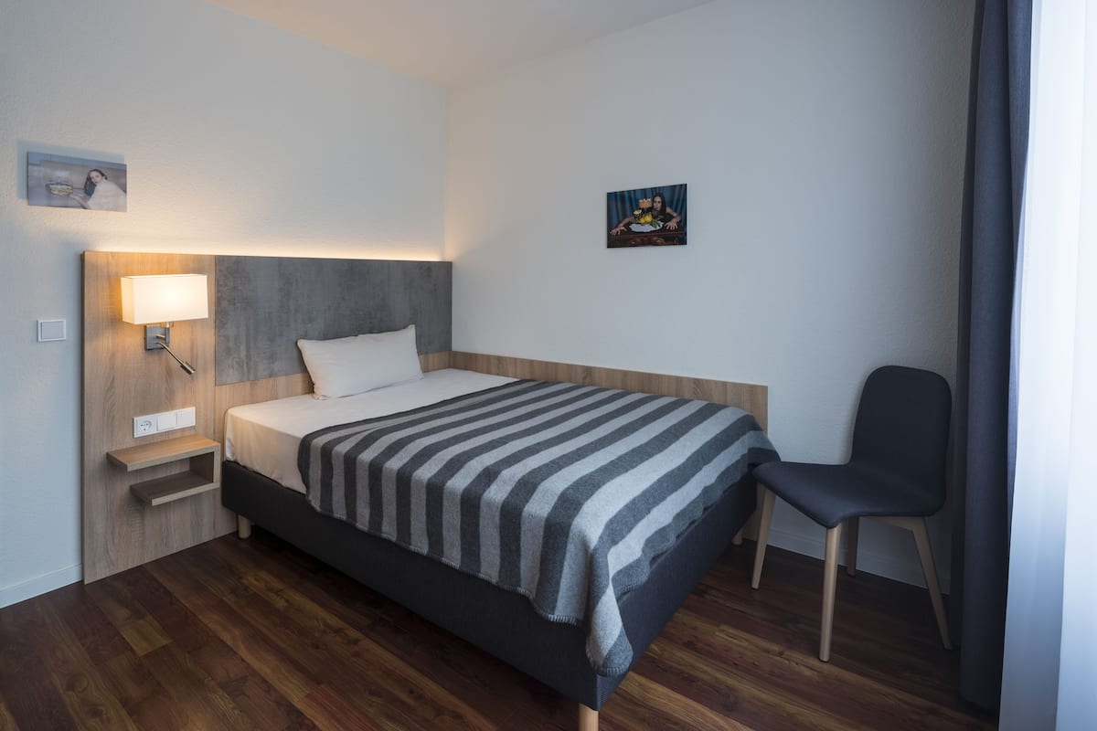 Ein modernes Hotelzimmer mit Bett, Nachttisch, Lampe, Sessel und einem Kunstwerk an der Wand.