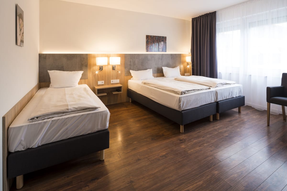 Ein Hotelzimmer mit zwei Betten, Holzboden und an der Wand befestigten Nachttischen mit Lampen.
