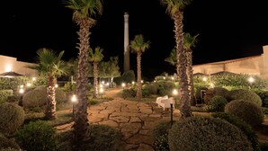 A nighttime garden with palm trees, a stone pathway, and a tall column. - Tonnara di Sciacca (Sciacca)