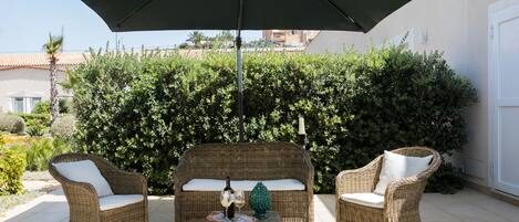 En patio med fletmøbler, et bord med en flaske og glas, samt en stor parasol.