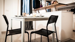 Une cuisine moderne avec un îlot central blanc, des chaises noires et une étagère en bois où sont disposés des fruits et une plante.