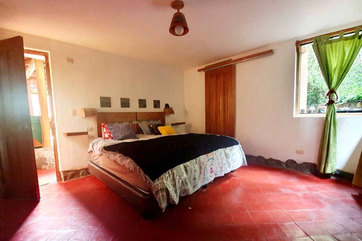 A bedroom with a bed, a wooden headboard, a window with curtains, and a red floor.