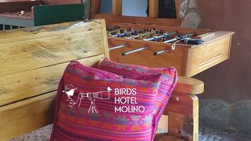 A wooden bench with a colorful pillow, a foosball table, and a stone wall with a rustic mirror.