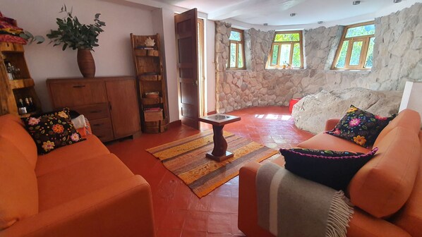 Una sala acogedora con sofás naranjas, una mesa de centro de madera y una pared de piedra.