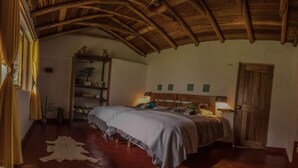 Une chambre confortable avec un plafond en bois, un lit doté d’une tête de lit, une table de chevet et une étagère ornée d’objets décoratifs.