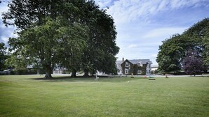 A grassy park area with a large tree and a building in the background. - Coolanowle Country House (Arless)
