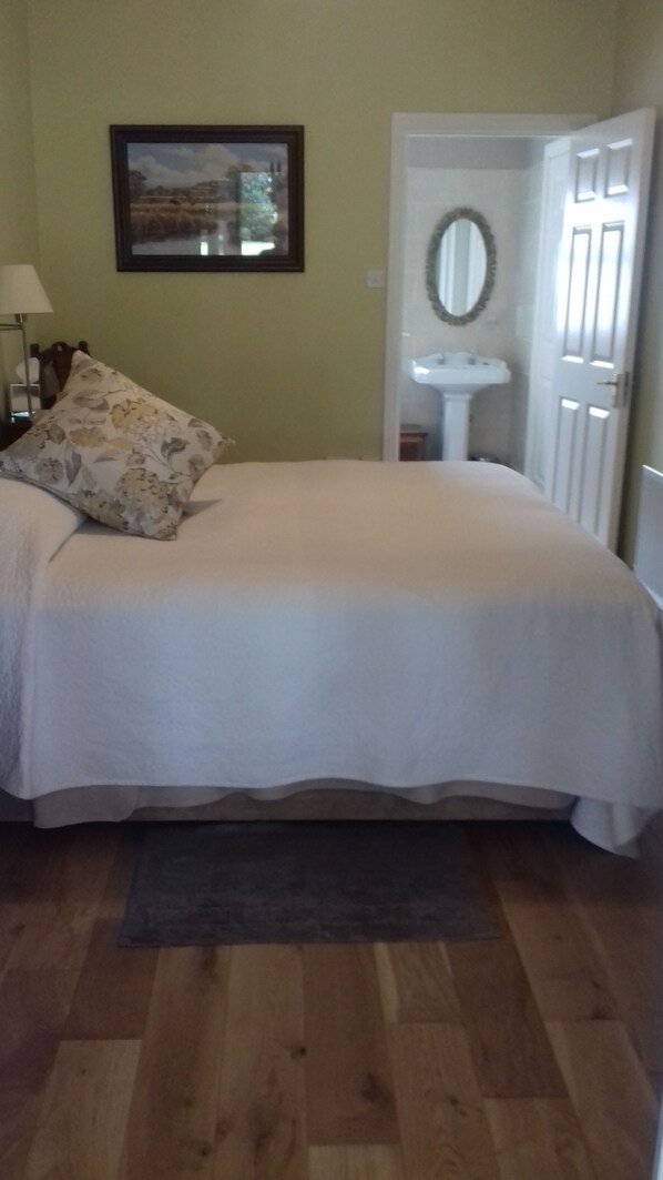 A bedroom with a bed, a nightstand, a lamp, a framed picture on the wall, a mirror, and a door leading to another room. - Coolanowle Country House (Arless)