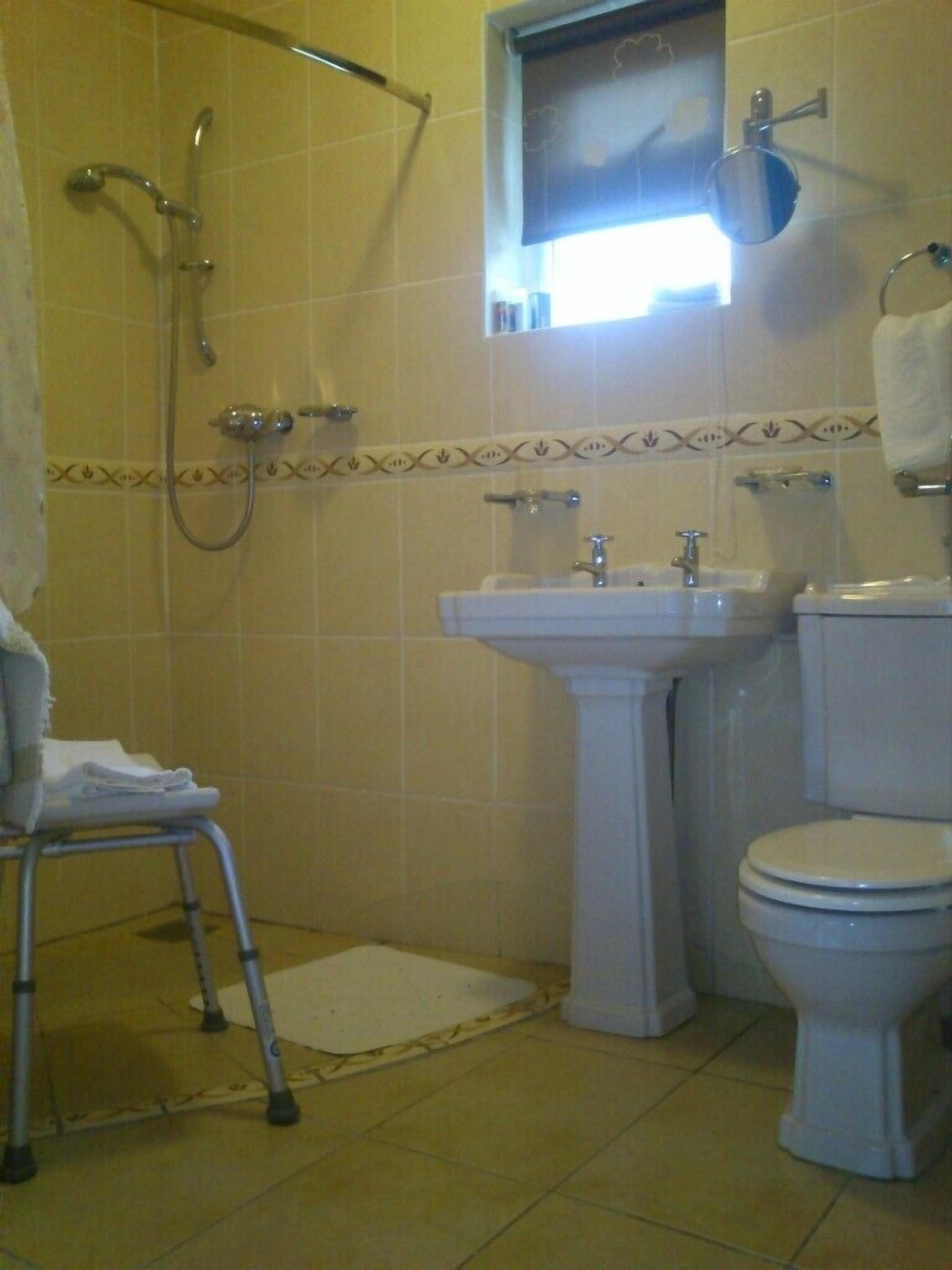 A bathroom with a shower, sink, toilet, and a small window.