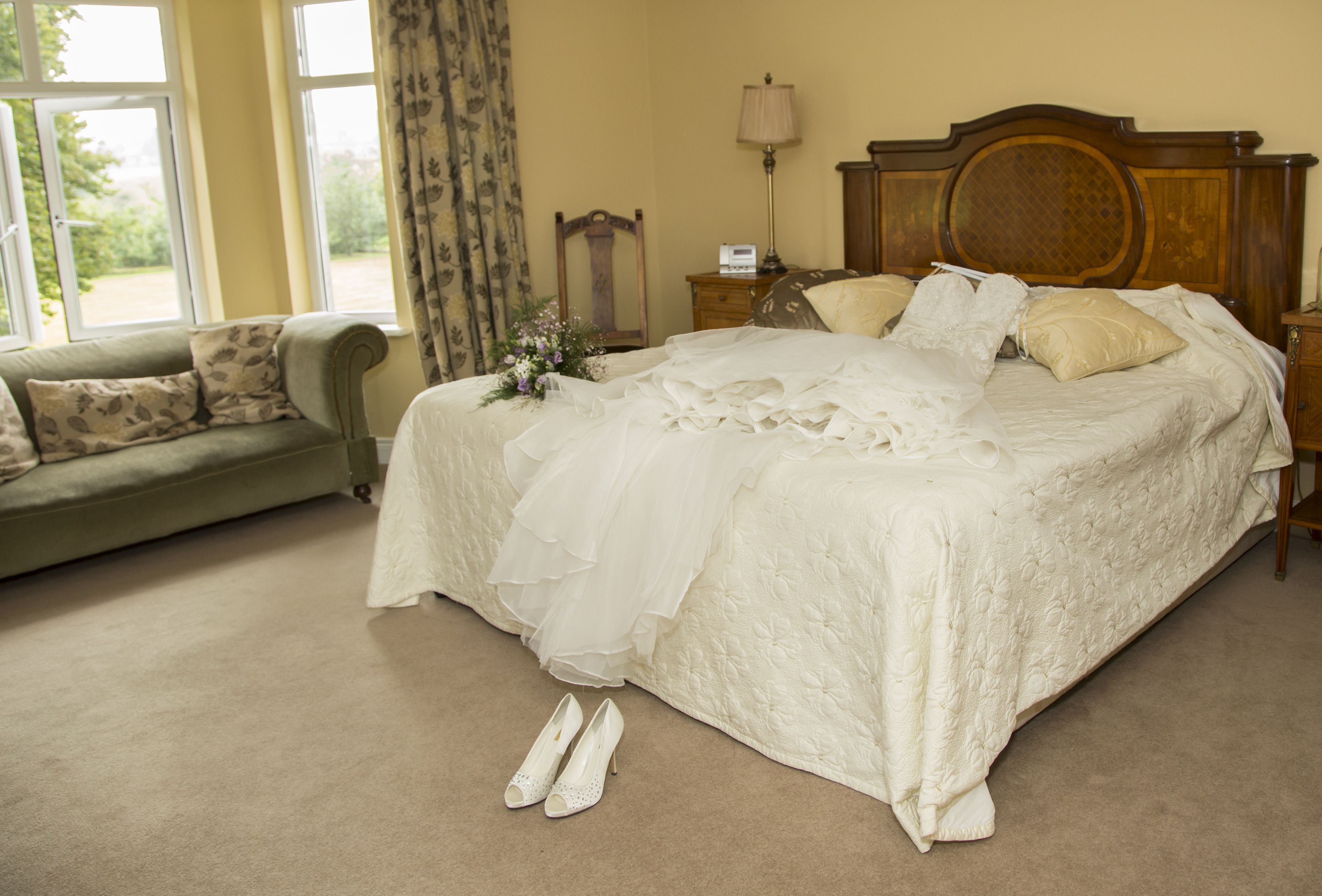 A neatly made bed with a white bedspread, a wooden headboard, and a nightstand with a lamp.