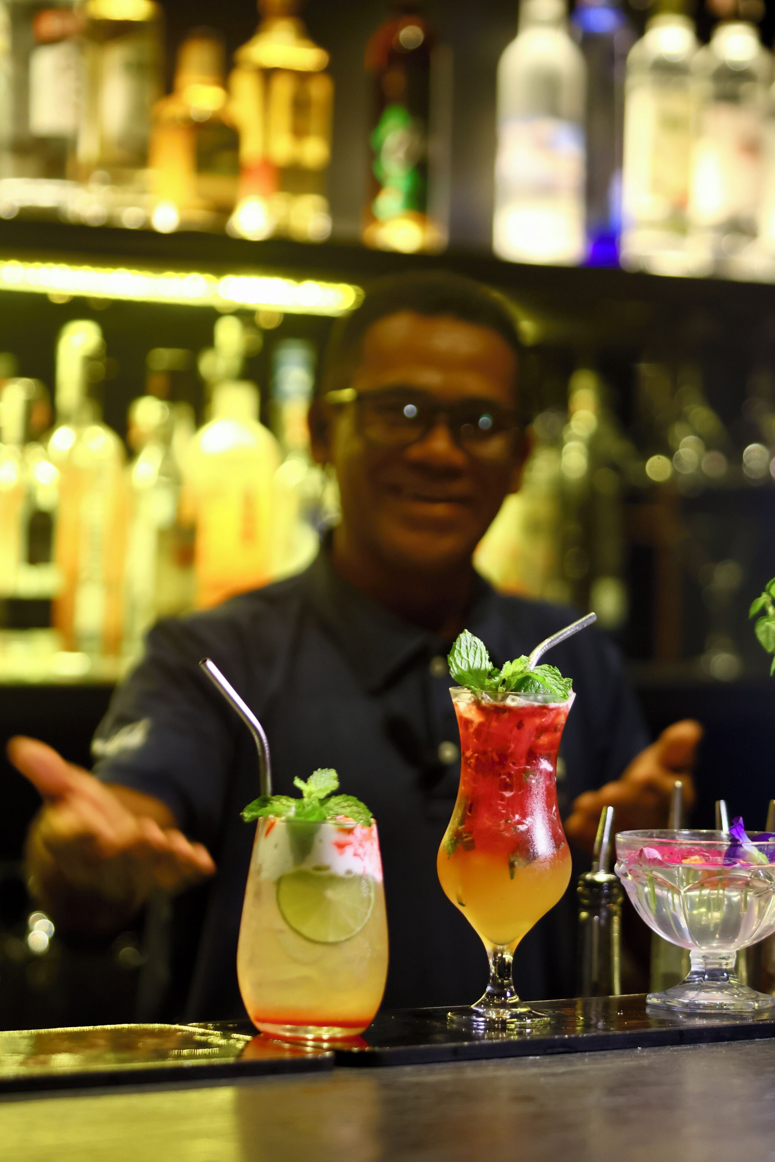 A bar setting with a bartender and three drinks on the counter.