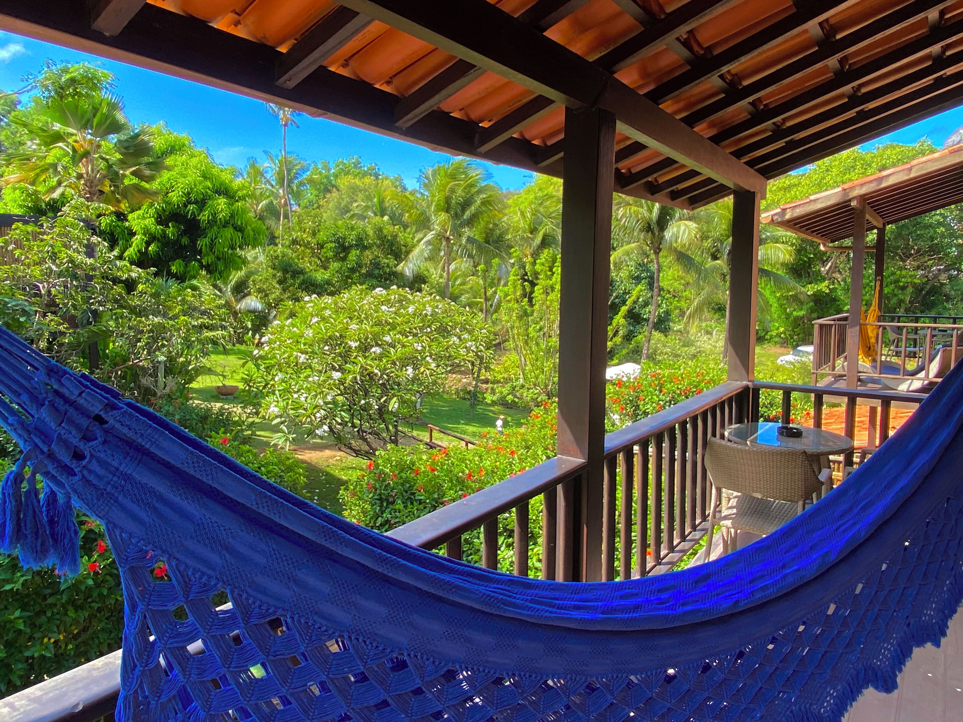 A hammock on a balcony overlooking a lush garden with a wooden pergola and outdoor furniture.