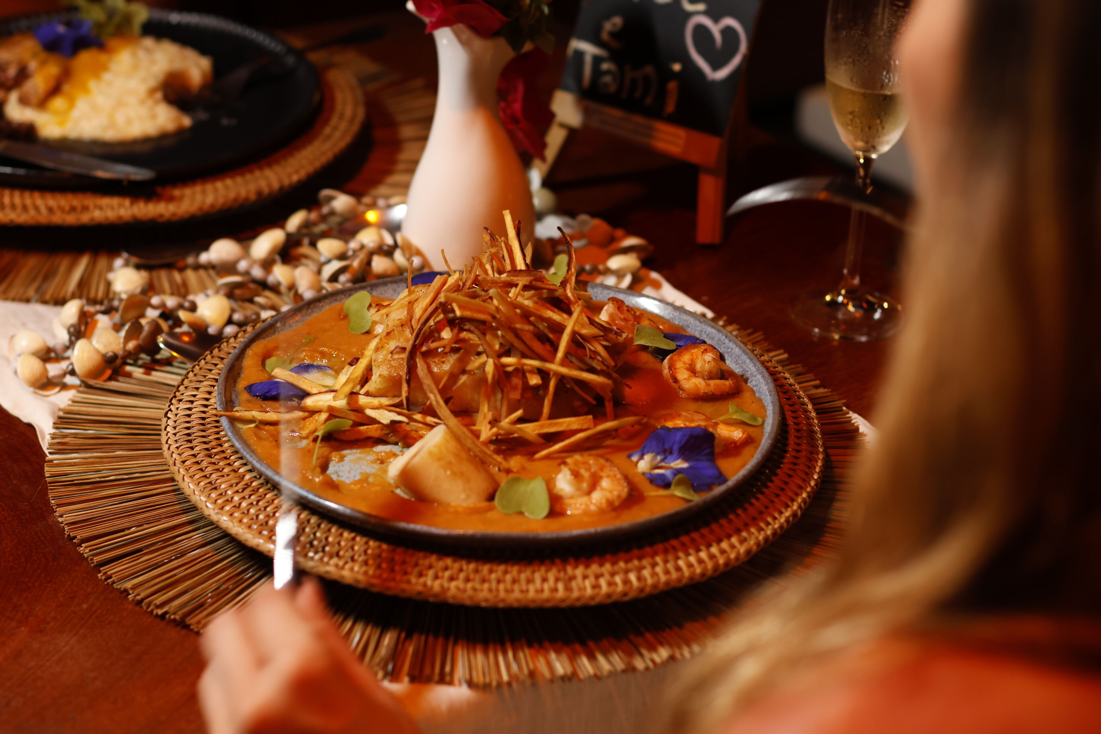 A dining table with a plate of food, a glass of wine, and a vase with a flower.