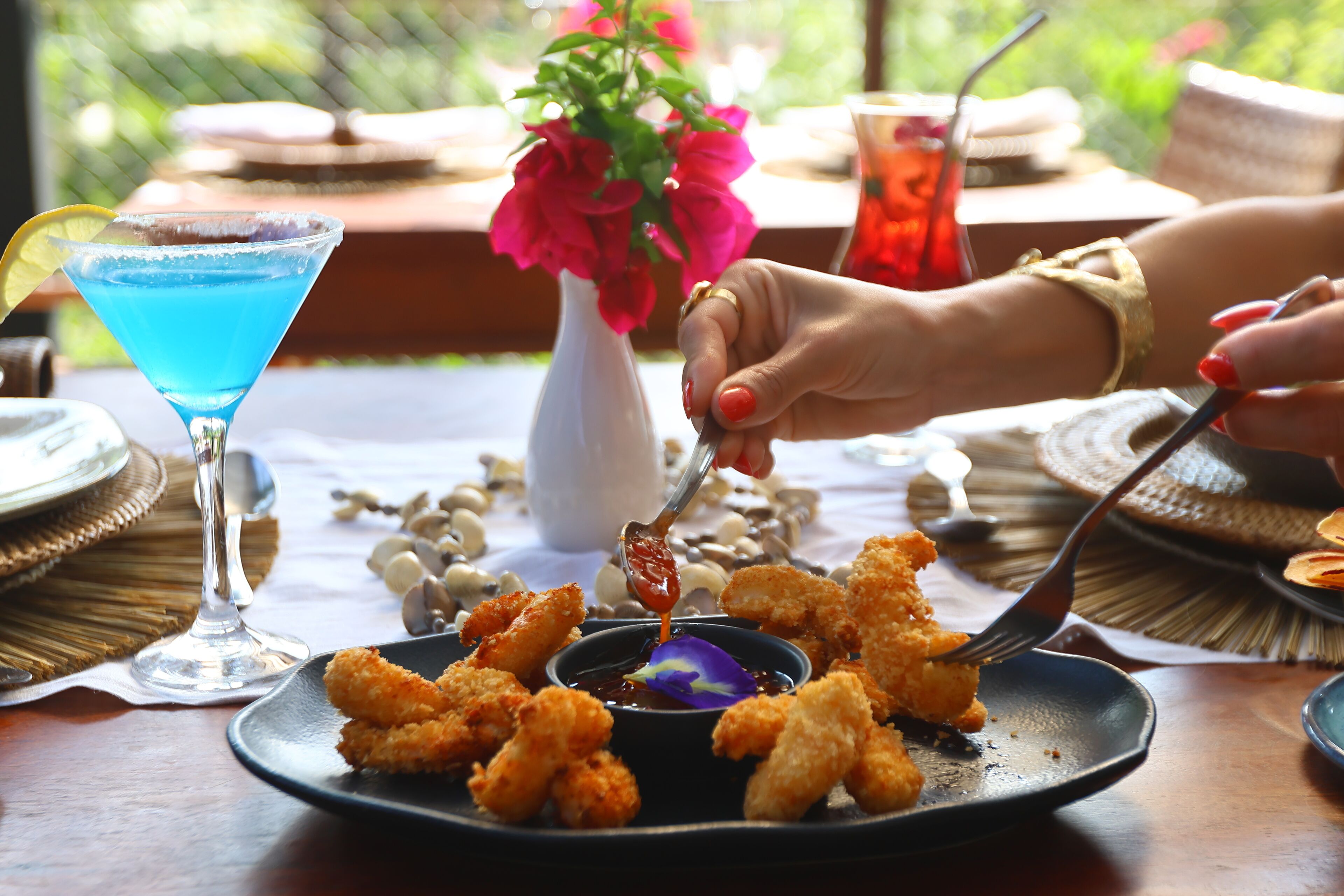 Une table à manger avec une assiette de nourriture frite, une boisson et un vase rempli de fleurs.